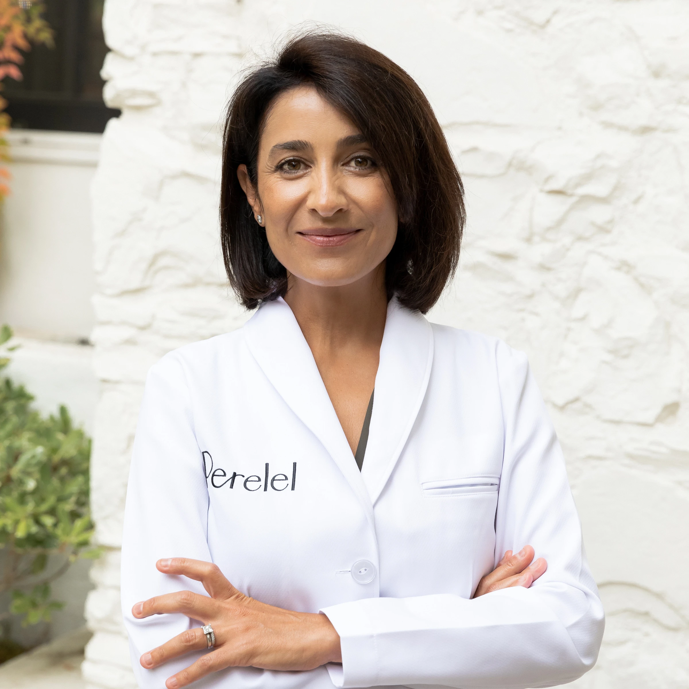 Dr. Banafsheh Bayati, board-certified OB/GYN, in a white coat embroidered with the Perelel name
