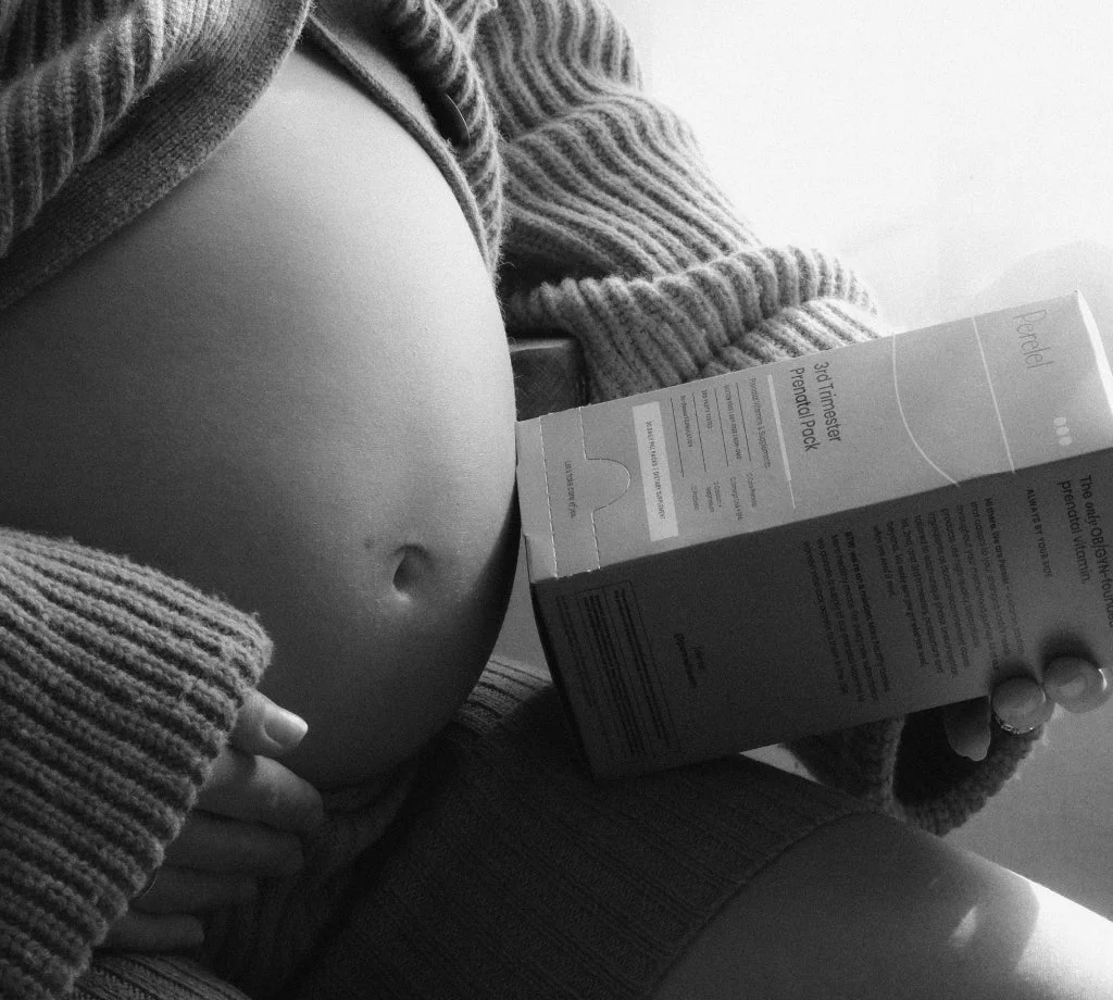 Black and white photo of a pregnant belly held by a woman in a knit sweater